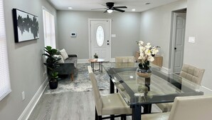 A modern dining area with a glass table, beige chairs, and a ceiling fan. - Cozy 2-bedroom cottage (New Orleans)