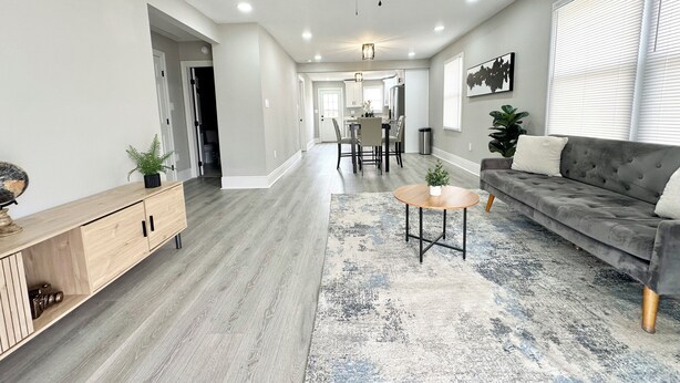 A spacious living room with a grey sofa, a coffee table, and a dining area in the background. - Cozy 2-bedroom cottage (New Orleans)