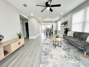 Uma sala de estar ampla com um sofá cinza, uma mesa de centro e um espaço de jantar ao fundo.