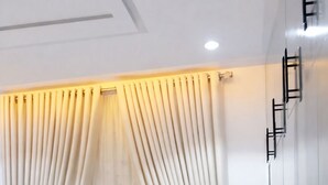 Ein Zimmer mit grauem Sofa, einem Fenster mit durchsichtigen Vorhängen und einer an der Wand befestigten Leiter.