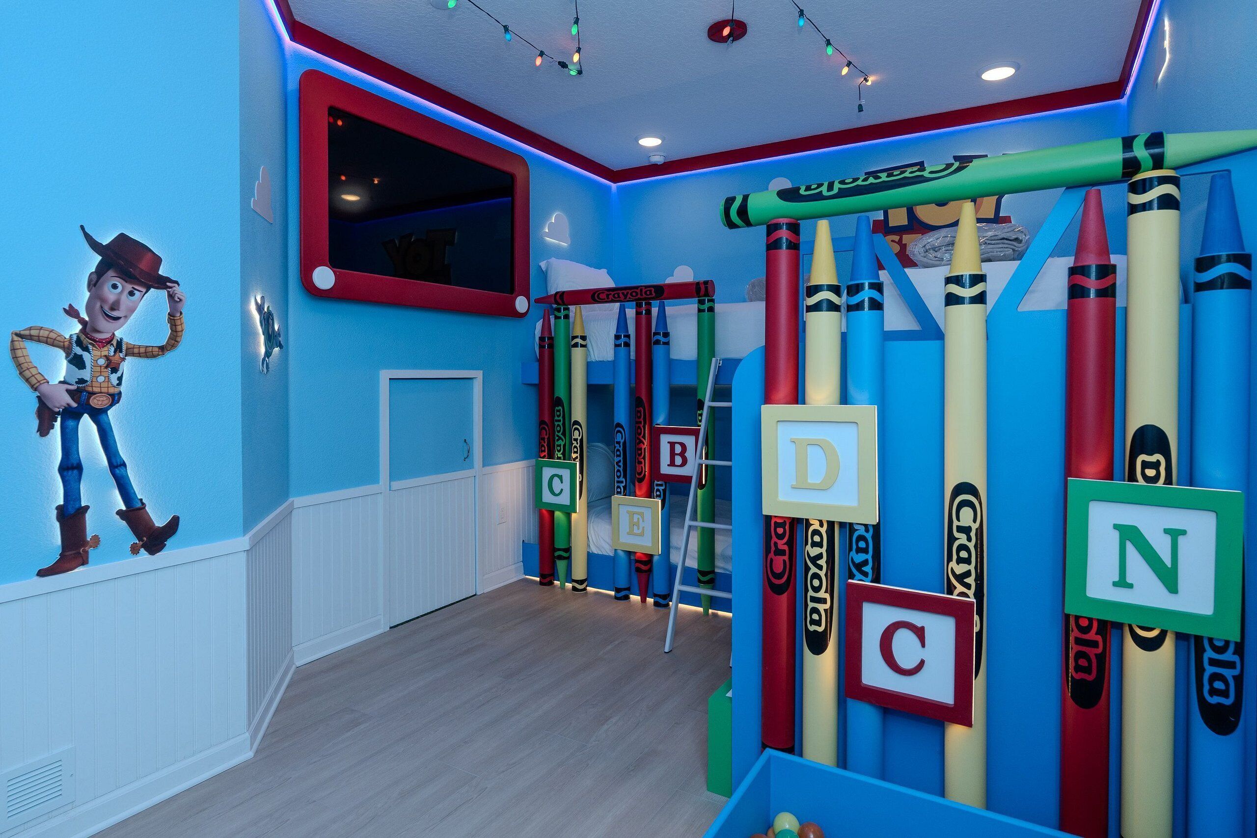 A children's playroom with a Woody the Cowboy mural, alphabet letters on crayons, and a window with blinds.