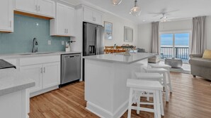 Une cuisine moderne avec des meubles blancs, un réfrigérateur en acier inoxydable et un grand îlot central doté de tabourets de bar.