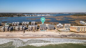 Vue aérienne d’un quartier résidentiel situé sur la côte, avec des propriétés donnant sur la plage, une marina et une vue dégagée sur l’océan.