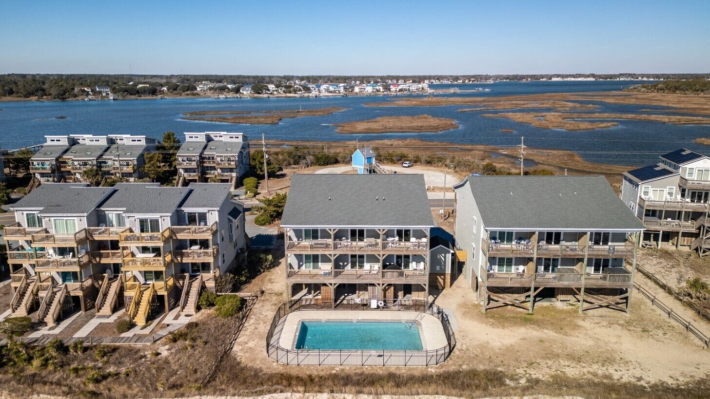 A coastal hotel with multiple-story buildings, a swimming pool, and a view of the water.