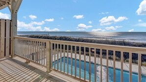 Une terrasse en bois avec une piscine, offrant une vue sur une plage et l’océan.