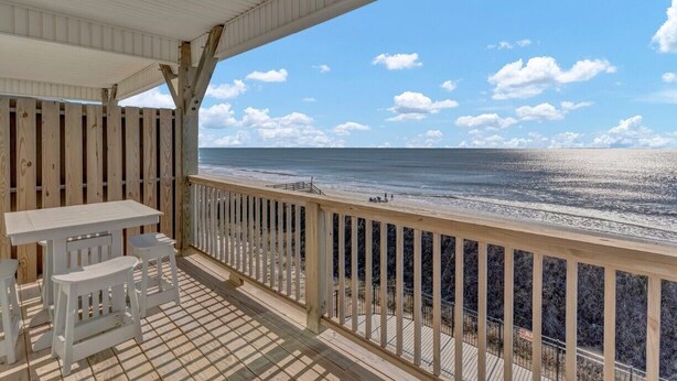 Une terrasse couverte avec vue sur la plage, des meubles en bois et une rambarde.