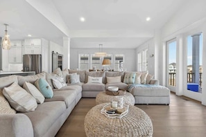 A spacious living room with a large sofa, a round coffee table, and a kitchen area in the background. - Endless Summer by Brunswick Vacation Rentals w/ Pool, Hot Tub & Walk To Beach (Ocean Isle Beach)