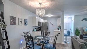 Eine moderne Küche mit weißen Schränken, einem Esstisch mit Stühlen, einer Chandelierleuchtre und Kunstwerken an den Wänden.