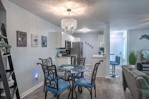 A modern kitchen with white cabinets, a dining table with chairs, a chandelier, and artwork on the walls. - South Bay East Unit H (Myrtle Beach)
