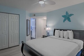 A bedroom with a bed, a nightstand, a lamp, a starfish decoration, and a door. - South Bay East Unit H (Myrtle Beach)