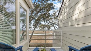 A covered porch with two blue chairs and a table with a plant, overlooking a field. - 2BR 2.5BA Marsh views Amenity Access (Seabrook Island)