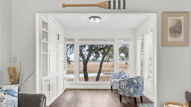 A room with a view of trees and water outside, a white cabinet with shelves, a patterned chair, and a wooden paddle on the ceiling. - 2BR 2.5BA Marsh views Amenity Access (Seabrook Island)