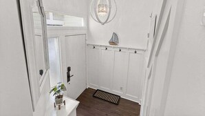 A hallway with a white door, a potted plant, a black mat, a decorative sailboat, and a chandelier. - 2BR 2.5BA Marsh views Amenity Access (Seabrook Island)