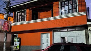 A two-story building with a red and white facade, a parked car in front, and visible power lines. - Karim Hostal Antigua (Guatemala City)