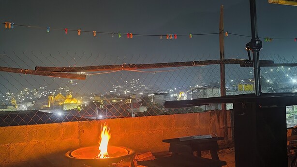 An outdoor seating area with a fire pit, tables, and chairs, overlooking a cityscape at night. - Karim Hostal Antigua (Guatemala City)