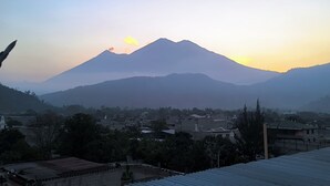 A mountain with a sunrise or sunset in the background, a town with buildings in the foreground, and a clear sky. - Karim Hostal Antigua (Guatemala City)