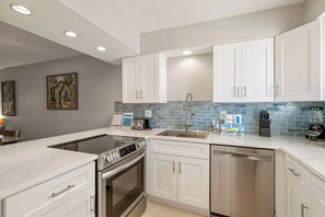A modern kitchen with white cabinets, a stainless steel dishwasher, a built-in oven, and a tiled backsplash. - Some Like It Hot at Runaway Bay 148 (Bradenton Beach)