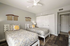 A bedroom with two beds, a ceiling fan, a wardrobe, and a door. - Some Like It Hot at Runaway Bay 148 (Bradenton Beach)