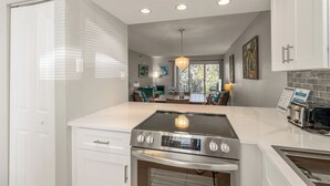 A modern kitchen with a built-in stove, oven, and toaster. There is a dining area with a table and chairs visible through the window. - Some Like It Hot at Runaway Bay 148 (Bradenton Beach)
