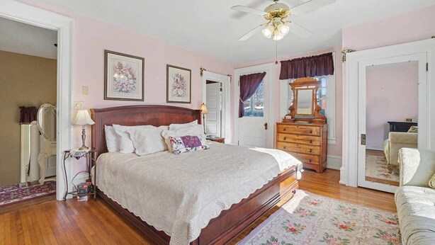 Une chambre à coucher avec un lit en bois, un ventilateur de plafond, une commode et un miroir.