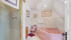 Une salle de bain avec une grande baignoire rose, des toilettes et un espace douche.