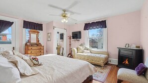 Une chambre à coucher avec un grand lit, une commode, une coiffeuse, une cheminée et une fenêtre avec des rideaux.