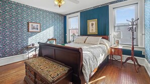 Een slaapkamer met bloemenbehang, een bed, een nachtkastje, een dressoir en een vloerlamp.