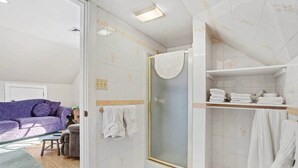 Un baño con ducha, inodoro y lavamanos. Hay un perchero con toallas y un estante con toallas dobladas.