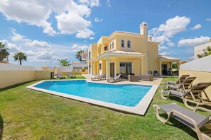 Une piscine avec des chaises longues, un bâtiment jaune doté d’un balcon et des palmiers.