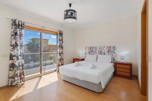 Ein Schlafzimmer mit einem großen Bett, einem Nachttisch, einer Lampe, einer Deckenleuchte und Blick ins Freie.