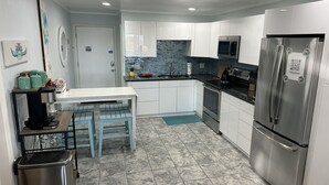 A modern kitchen with white cabinets, stainless steel appliances, and a tiled floor. - The Tiki Hut- 2 Bed, 2 Bath Oceanview Shore Drive Condo (Myrtle Beach)