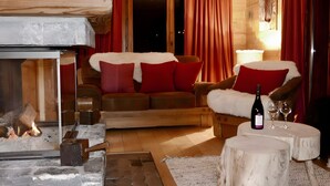 Interior acogedor de una cabaña de madera con chimenea, muebles de madera y una botella de vino sobre una mesa.