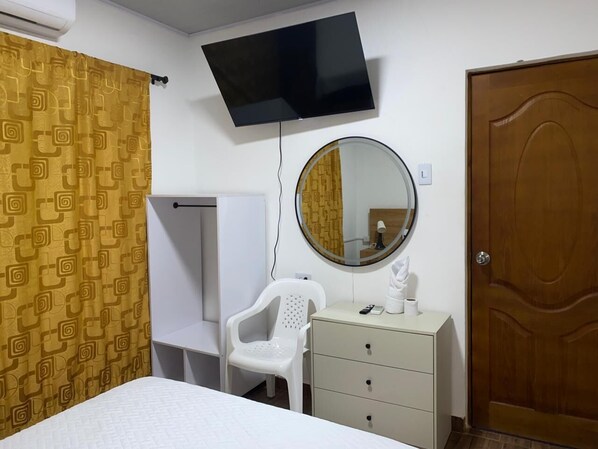 Un dormitorio con una cama, un televisor montado en la pared, un espejo redondo, un aparador y una puerta.