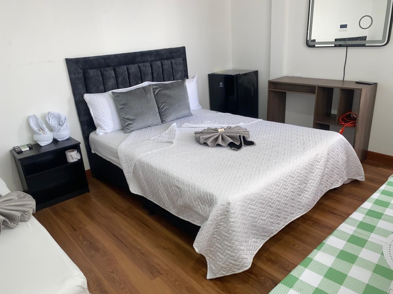 Un dormitorio ordenado con cama, mesitas de noche, un pequeño armario y un espejo en la pared.