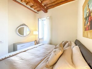 A bedroom with a bed, a dresser, a mirror, a window with curtains, and a painting on the wall. - Michelangelo Heart of Tuscany (Peccioli)