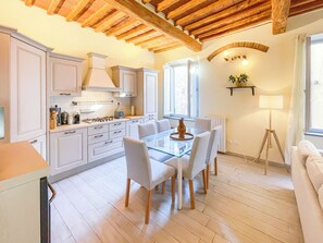 A modern kitchen with white cabinets, a glass dining table, and a wooden ceiling. - Michelangelo Heart of Tuscany (Peccioli)