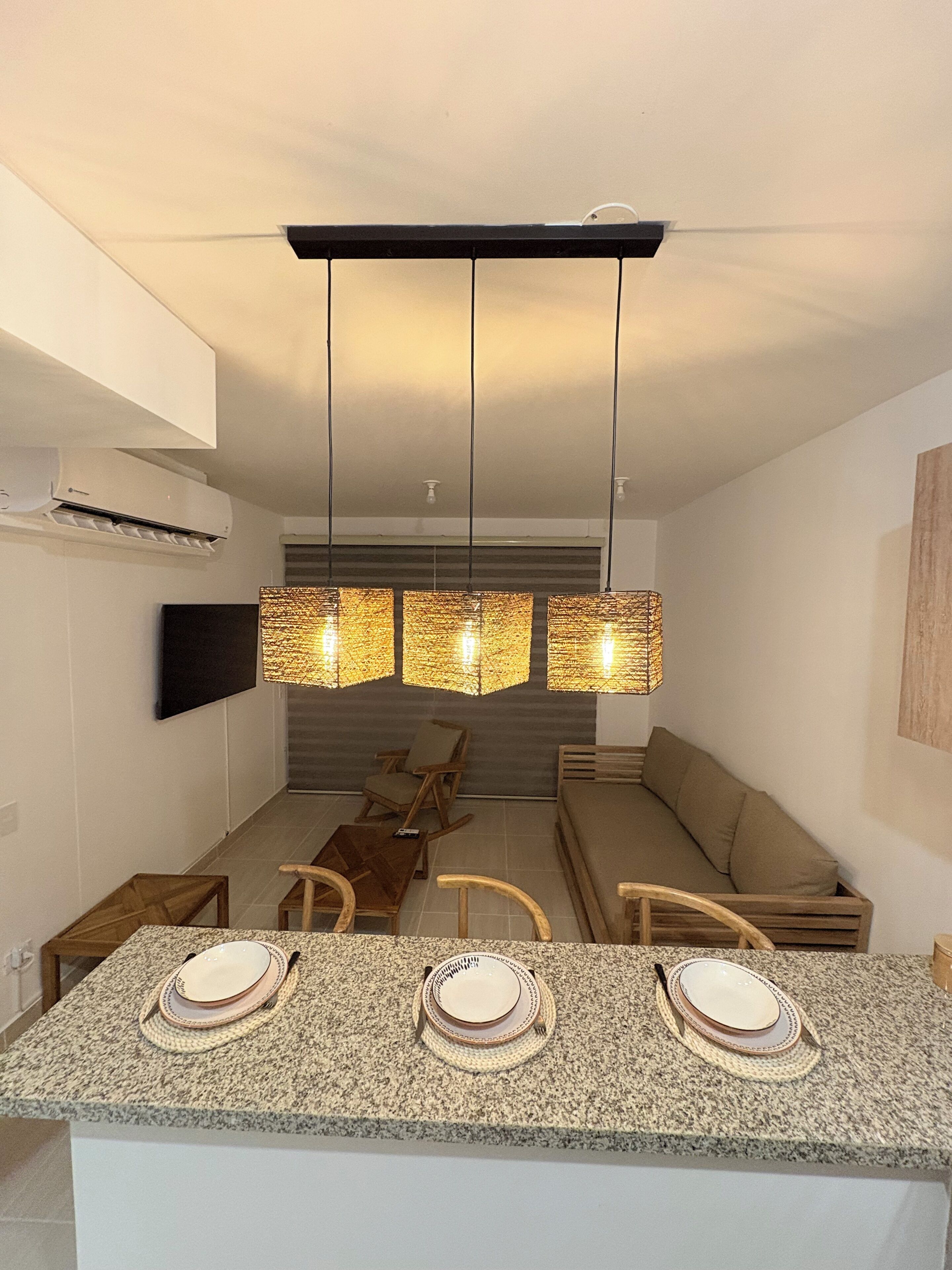 A modern kitchen with a granite countertop, three pendant lights, a built-in oven, and a dining area with a sofa and chairs.