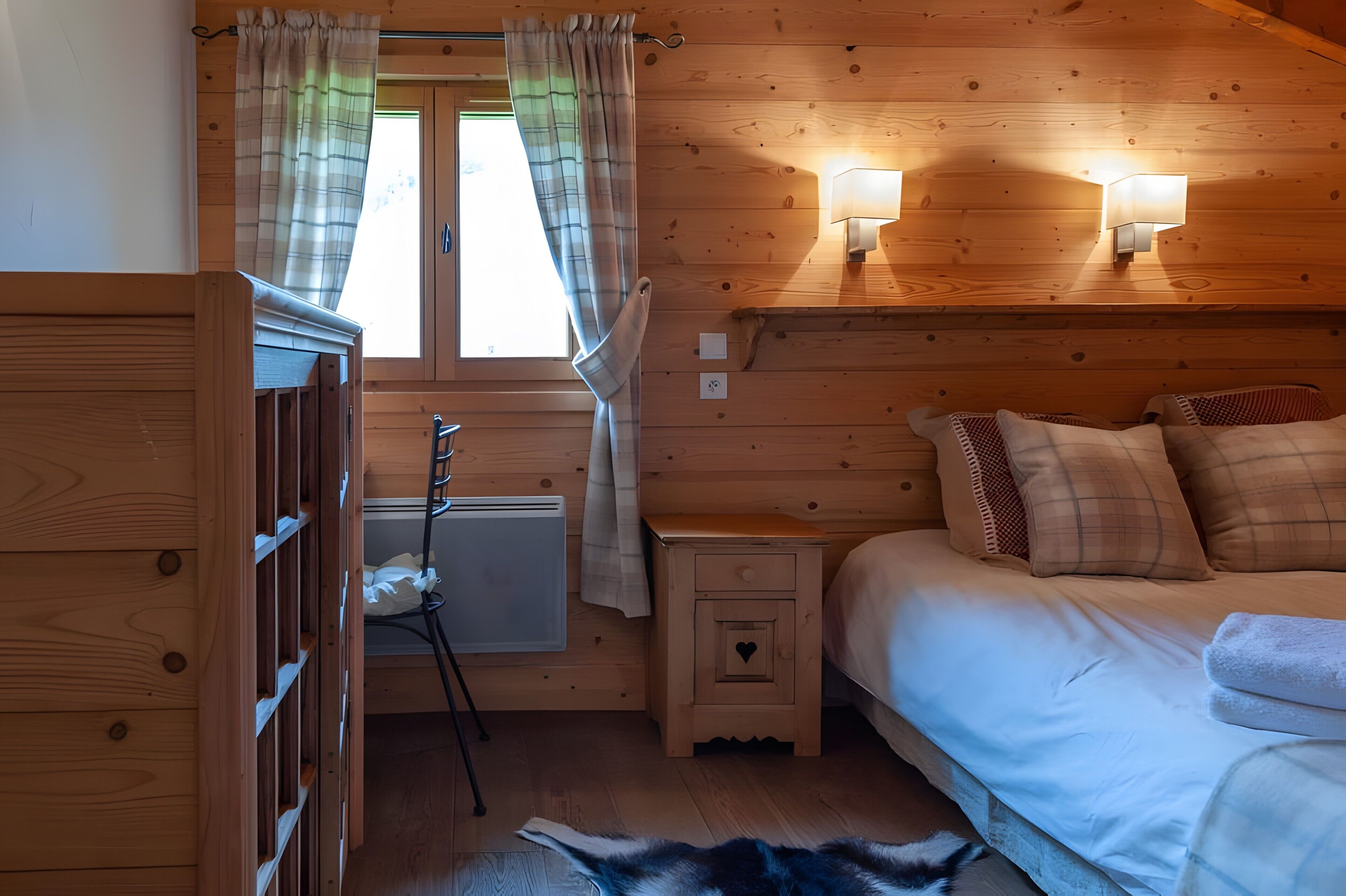 Een slaapkamer in een houten hutje, met een bed, bedlampjes, een nachtkastje, een radiator en een raam met gordijnen.
