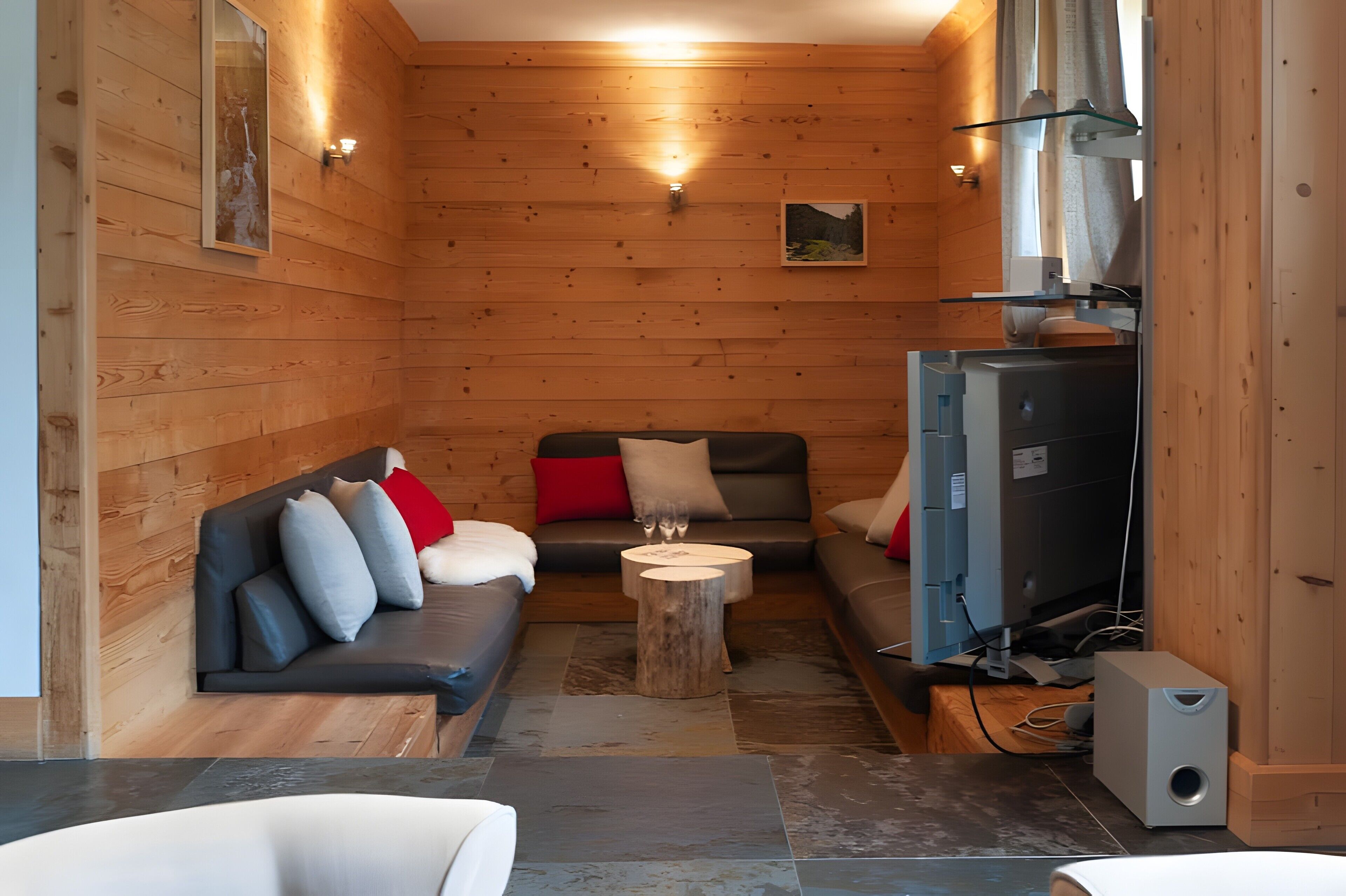 L’intérieur d’un chalet accueillant, avec des murs en bois, un canapé, une petite table et un téléviseur.