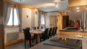 A modern kitchen with a central island, a dining area with chairs, and a view of a bathroom. - Chalet “Eden” with Balcony and Wi-Fi (Les Belleville)