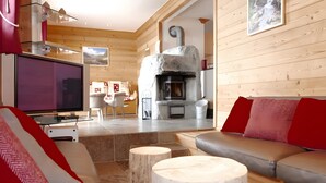 A modern living room with a stone fireplace, wooden walls, a leather sofa, and a television. - Chalet “Eden” with Balcony and Wi-Fi (Les Belleville)
