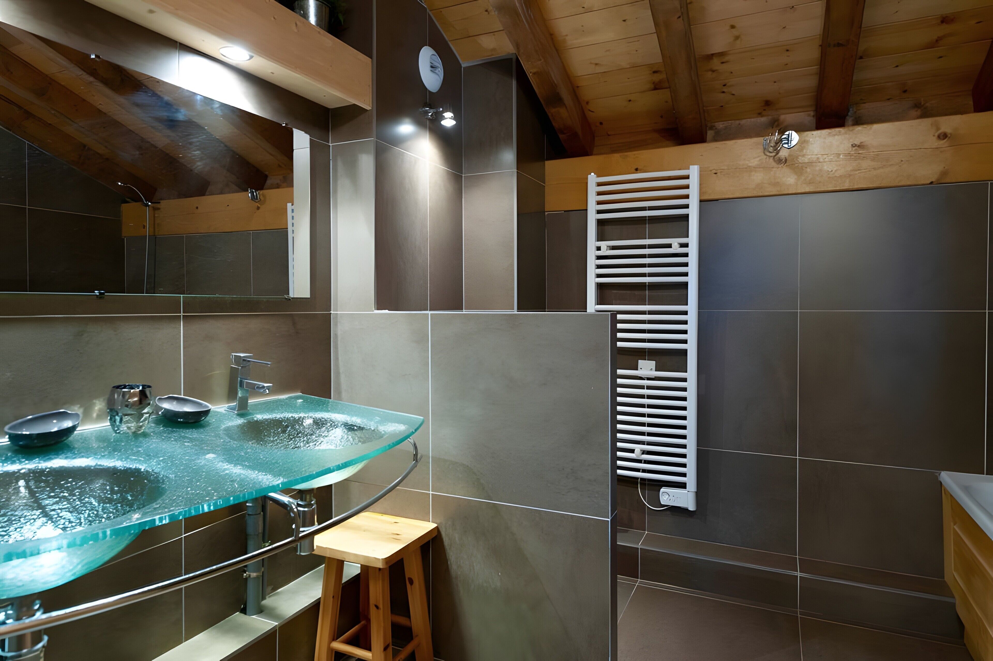 A bathroom with a glass sink, a wooden stool, a towel rack, and a mirror.