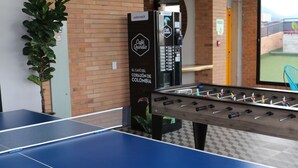 Ein Fußballtisch und ein Tischtennisplatte in einem Raum mit Backsteinwänden und einem großen Fenster.