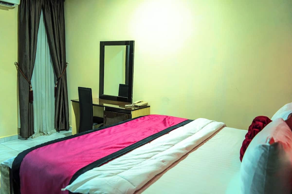 Una habitación de hotel con cama, escritorio, teléfono, espejo y cortinas.
