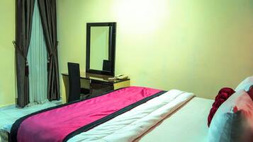 Una habitación de hotel con cama, escritorio, teléfono, espejo y cortinas.