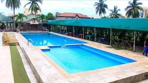 Une piscine rectangulaire dont le bord est recouvert de carreaux, entourée d’une zone abritée avec des chaises et agrémentée d’une petite cascade.