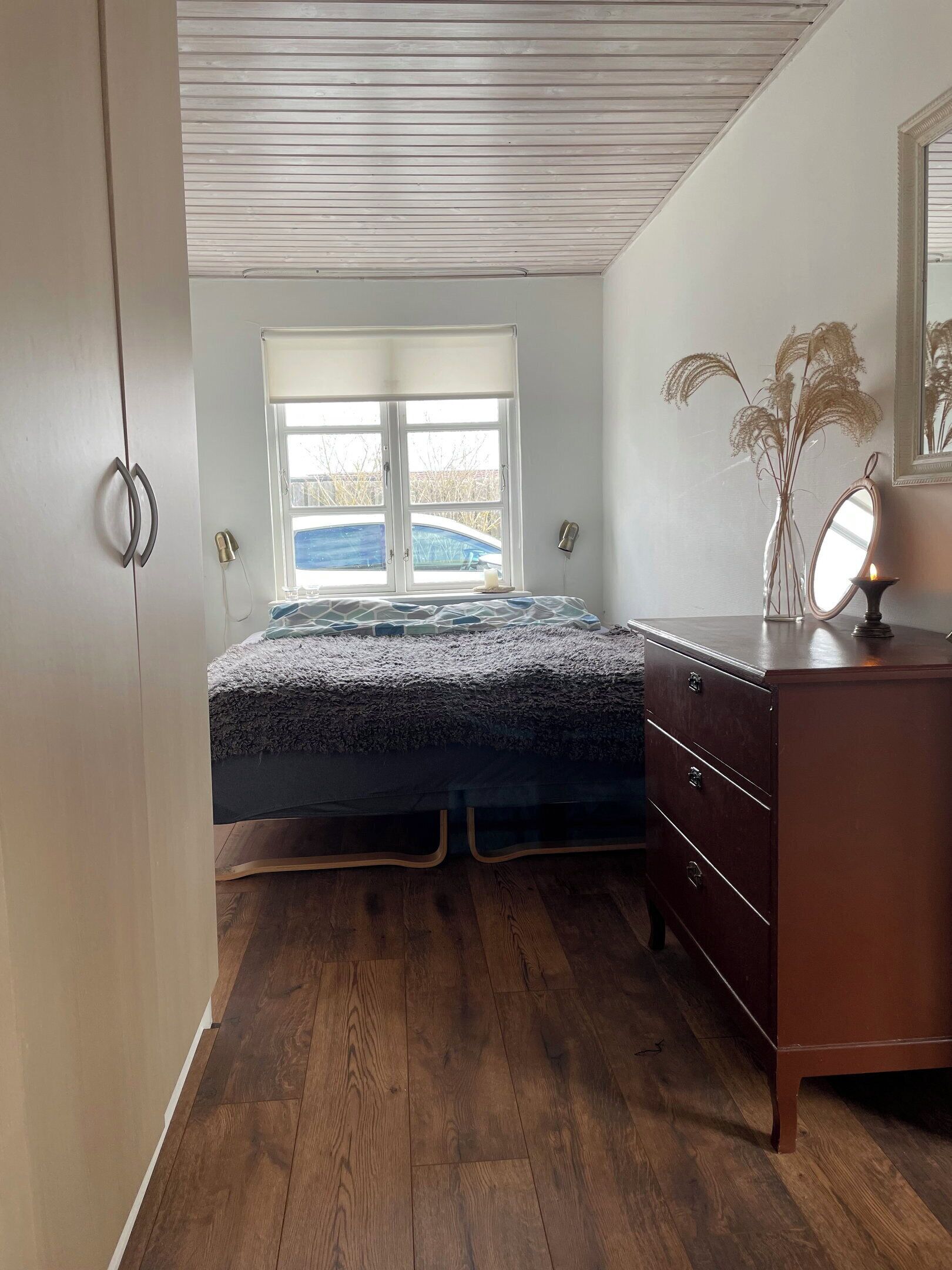A bedroom with a bed, a dresser, a window, and a mirror.