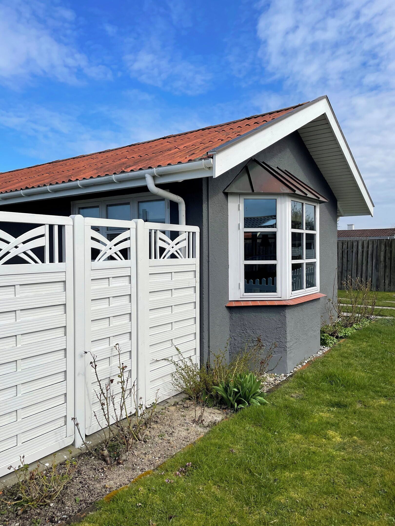 A residential house with a red-tiled roof, a white fence, and a small garden area.