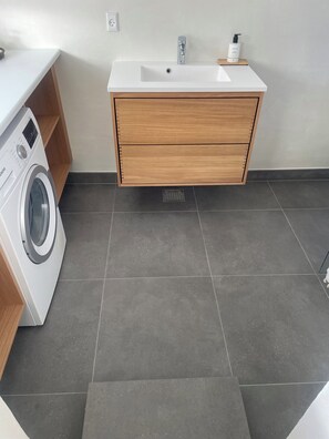 A modern bathroom with a white sink, wooden vanity, and a front-loading washing machine. - Lovely holiday home 80 m from the water (Otterup)
