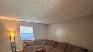 A living room with a L-shaped sectional sofa, a small table, and a window with blinds. - Near Fort Sill Cozy 2-Bedroom Townhouse (Lawton)